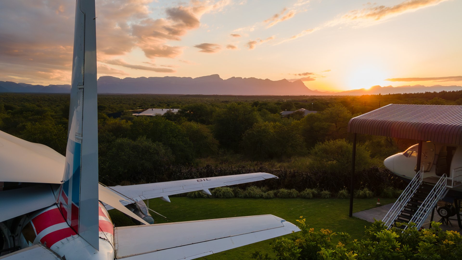Sunset view of Aerotel aircraft with Drakensberg mountains in background, showing Boeing 737 tail and entrance stairs